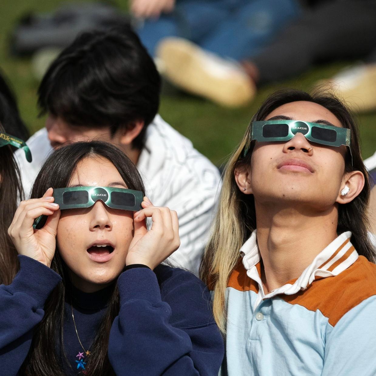 Two+students+watch+the+eclipse+through+Skidmore-branded+glasses.